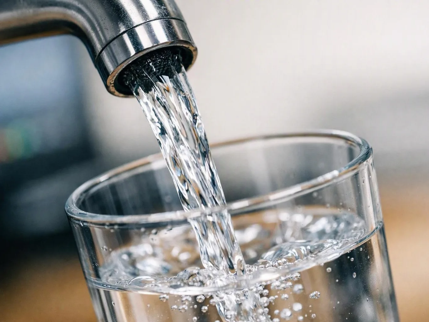 A chrome faucet pours clear water into a glass in a close-up kitchen scene