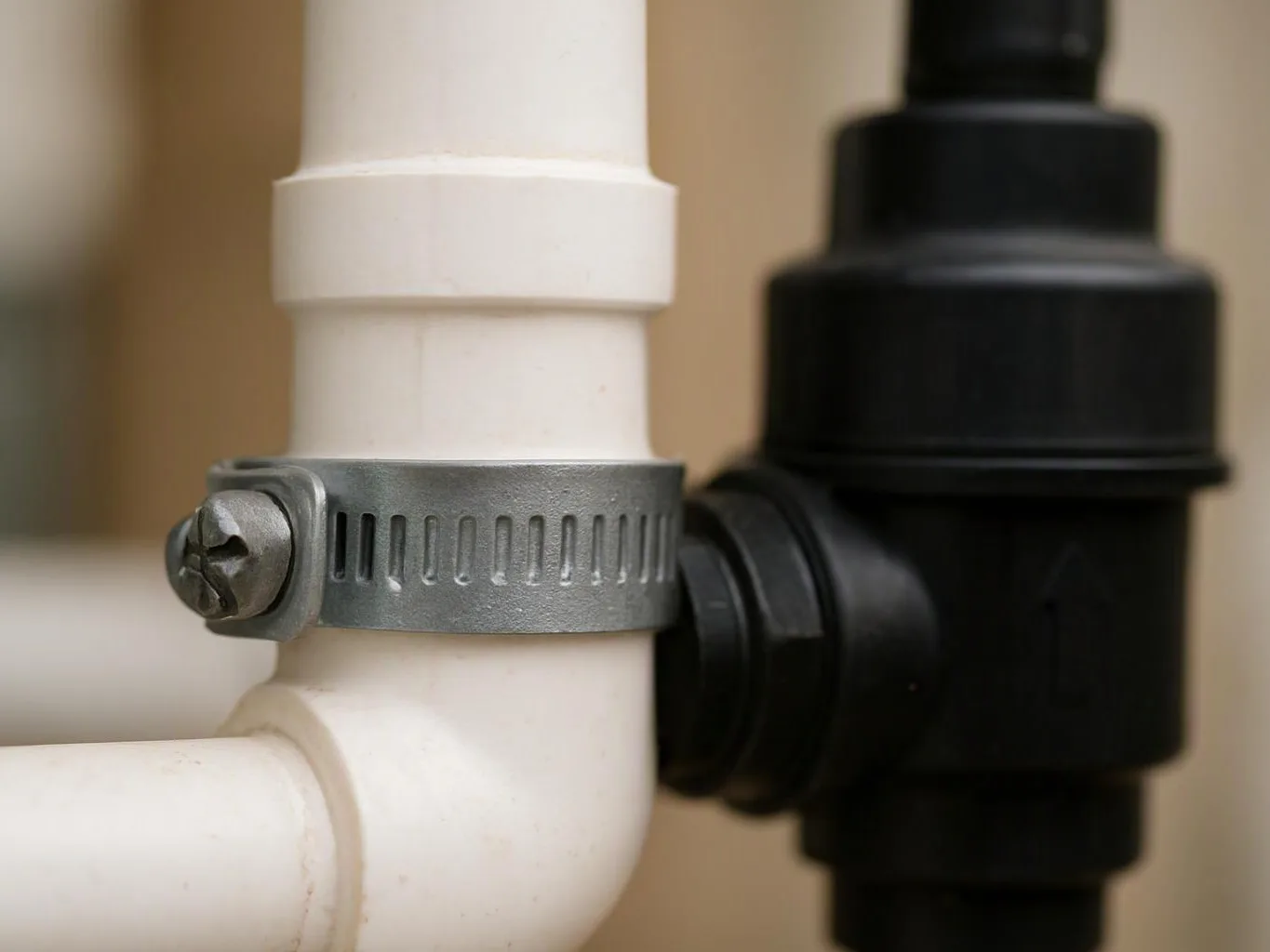 Close-up of white and black plastic pipes joined by a metal hose clamp against a beige background