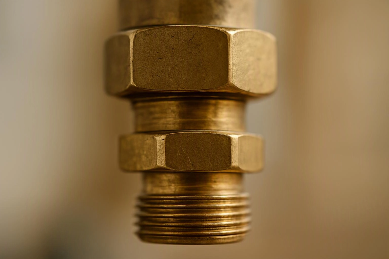Close-up of a brass pipe fitting with hex nuts and threaded end against a blurred beige background
